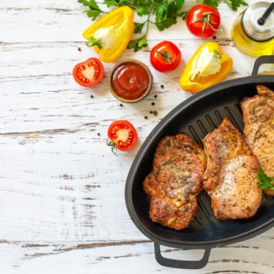 Baked pork chops in skillet on white wood surface.