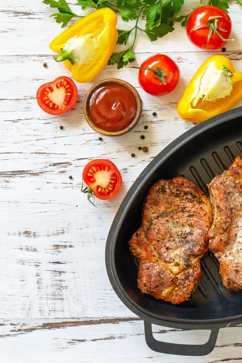 Baked pork chops in skillet on white wood surface. 