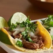 Three carna asada tacos on a serving dish.