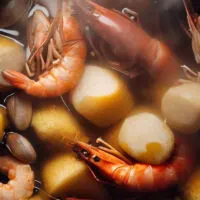 Top view of shrimp boil with potatoes and corn in pot.