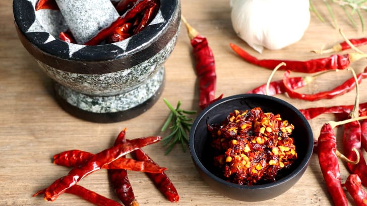 Red chilis and mortar and pestle on wooden surface.