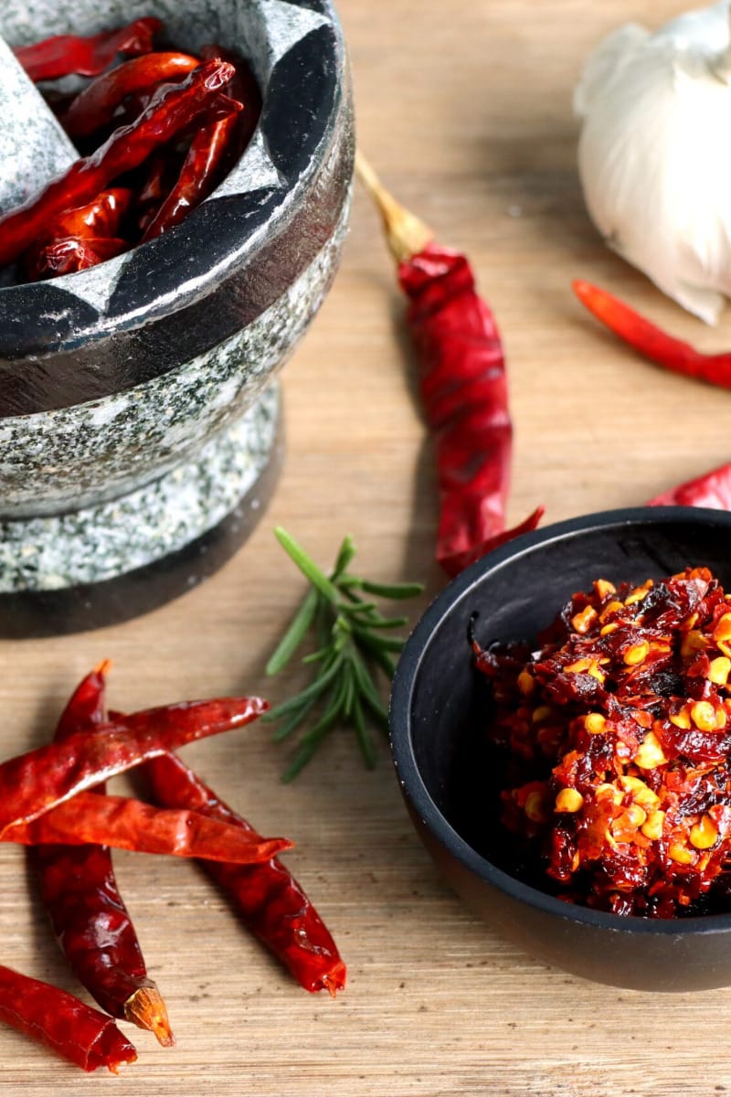 Red chilis and mortar and pestle on wooden surface.