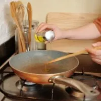 Close up of hand pouring oil into stovetop pan.