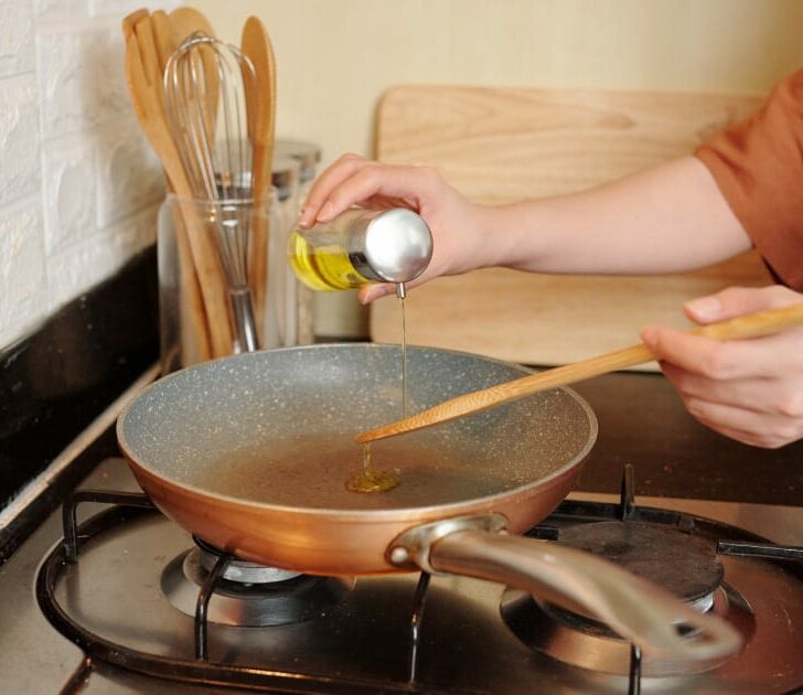 Close up of hand pouring oil into stovetop pan.