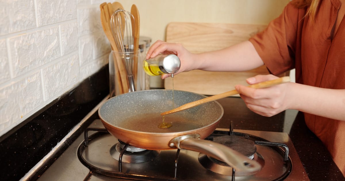 Close up of hand pouring oil into stovetop pan.