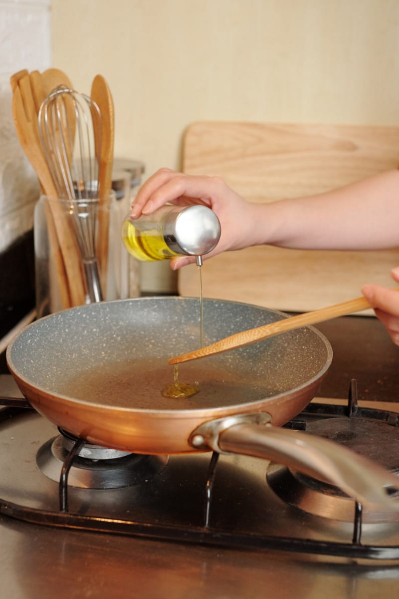 Close up of hand pouring oil into stovetop pan.