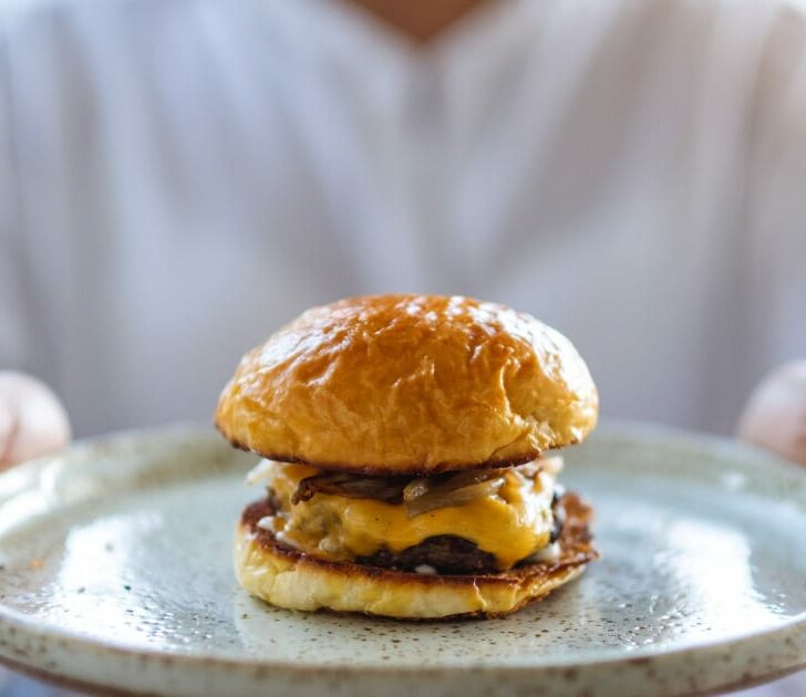 Close-up of woman holding tray with hamburger on it.