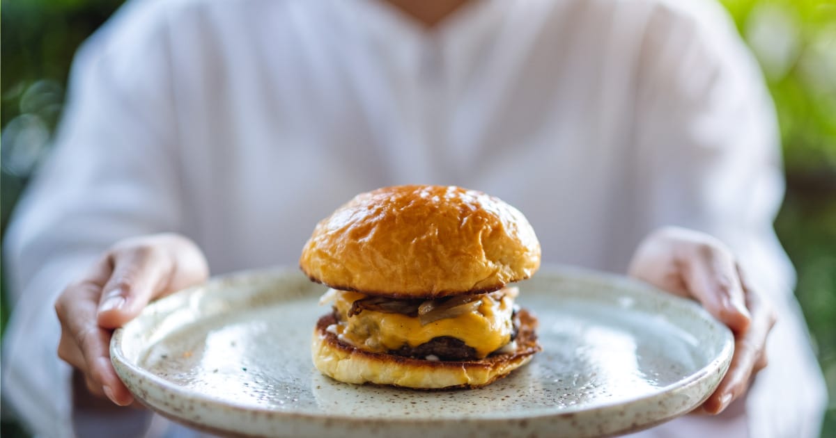 Close-up of woman holding tray with hamburger on it.