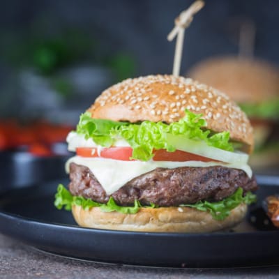 Side view of prepared hamburger on bun with cheese, lettuce, and tomato.