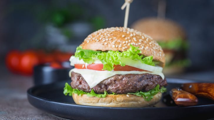 Side view of prepared hamburger on bun with cheese, lettuce, and tomato.