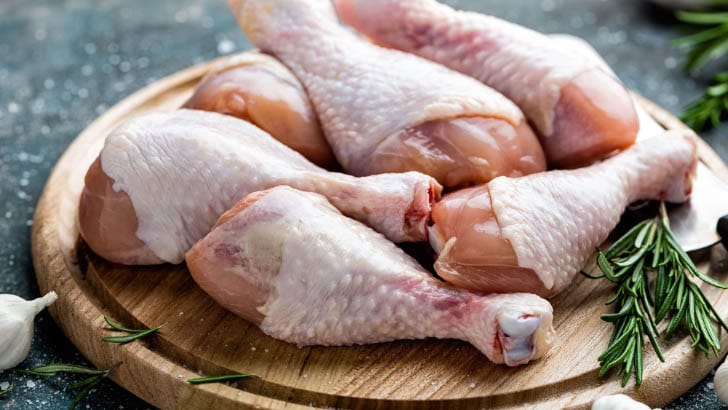 Raw chicken drumsticks on a cutting board.