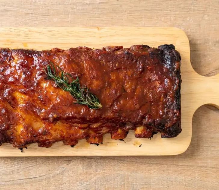 Cooked pork ribs on wooden serving plate.