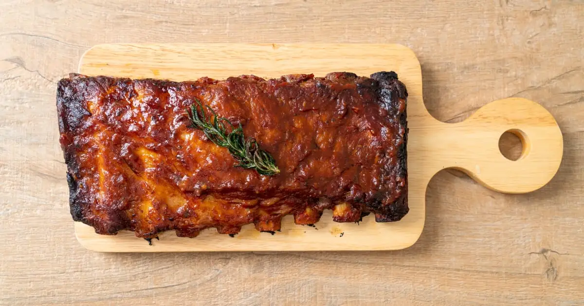 Cooked pork ribs on wooden serving plate.