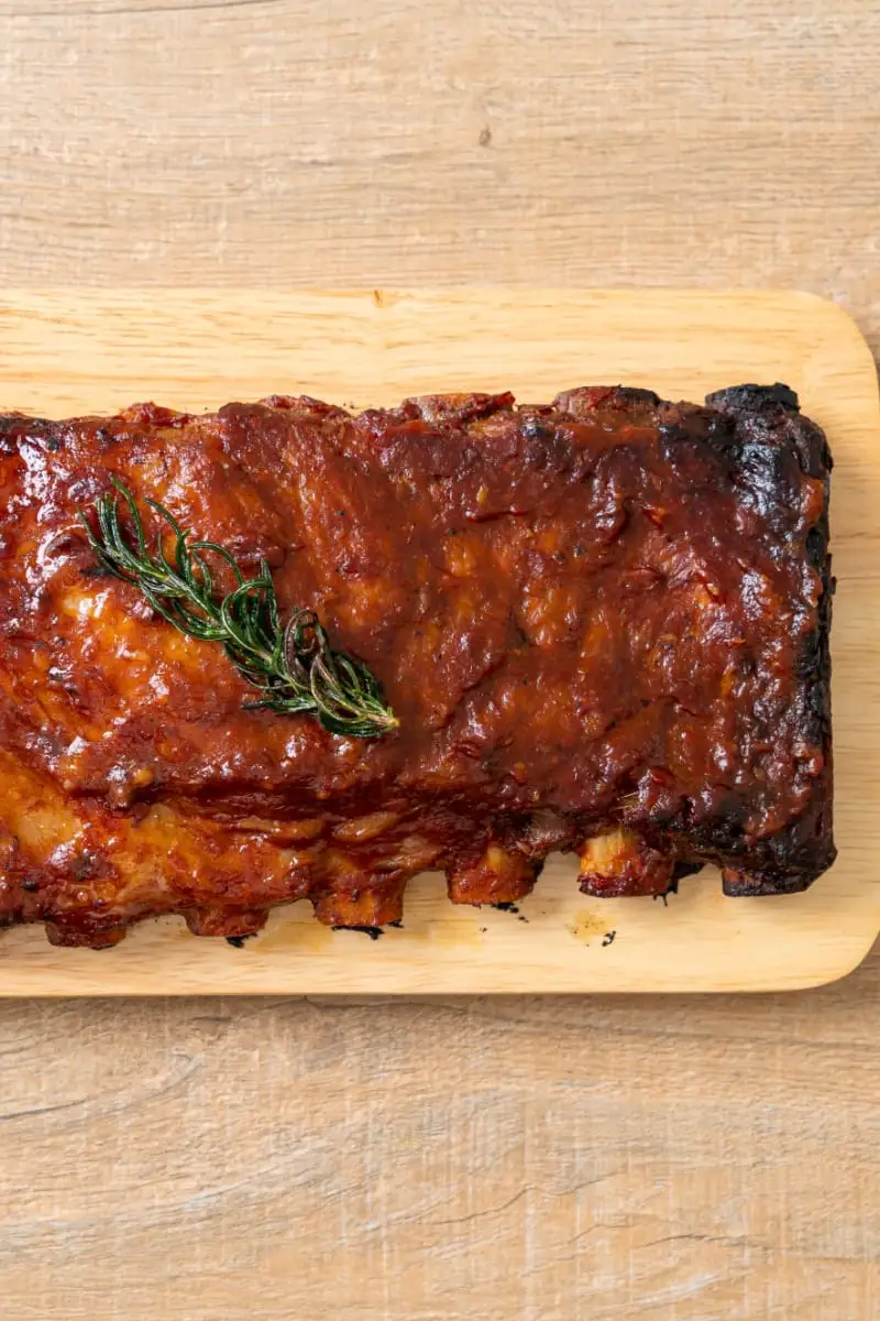 Cooked pork ribs on wooden serving plate.