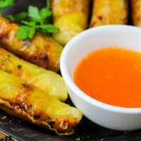 Fried eggrolls on serving dish with duck sauce as dipping condiment.