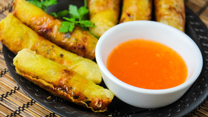 Fried eggrolls on serving dish with duck sauce as dipping condiment.