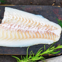 Overview view of cooked cod on wooden platter.