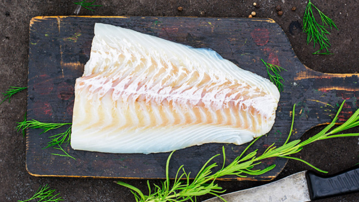 Overview view of cooked cod on wooden platter.