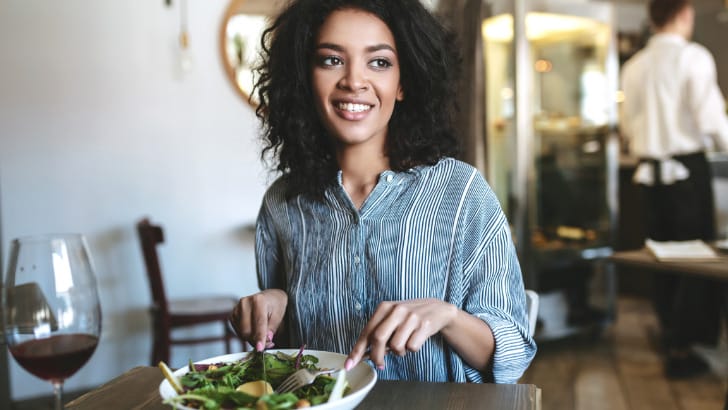 Smiling woman eats in a restaurant to represent NY restaurants that accept bitcoin.