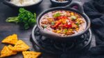 Bowl of chili con carne with rice and toppings on wooden table.