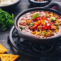 Bowl of chili con carne with rice and toppings on wooden table.