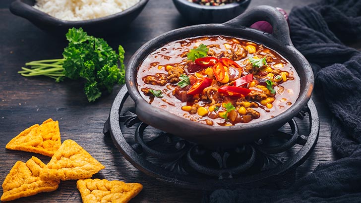 Bowl of chili con carne with rice and toppings on wooden table.