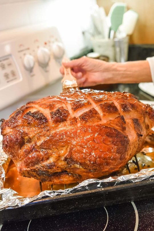 Close up of chef using a brush to glaze a precooked ham. 