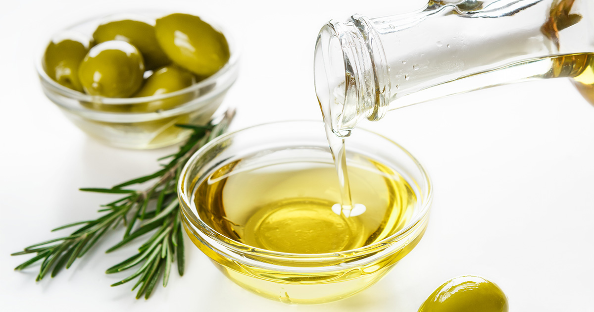 Olive oil pours from glass container into bowl.