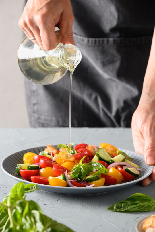 Person pours oil over tomato salad.