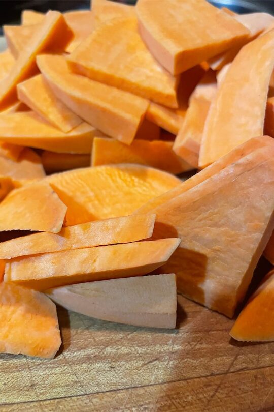 Yams cut into wedges on cutting board.