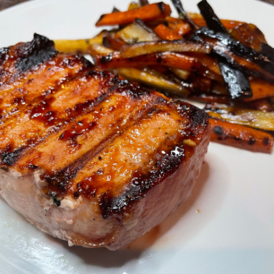 Honey garlic grilled pork chop on white plate with roasted carrots and parsnips.