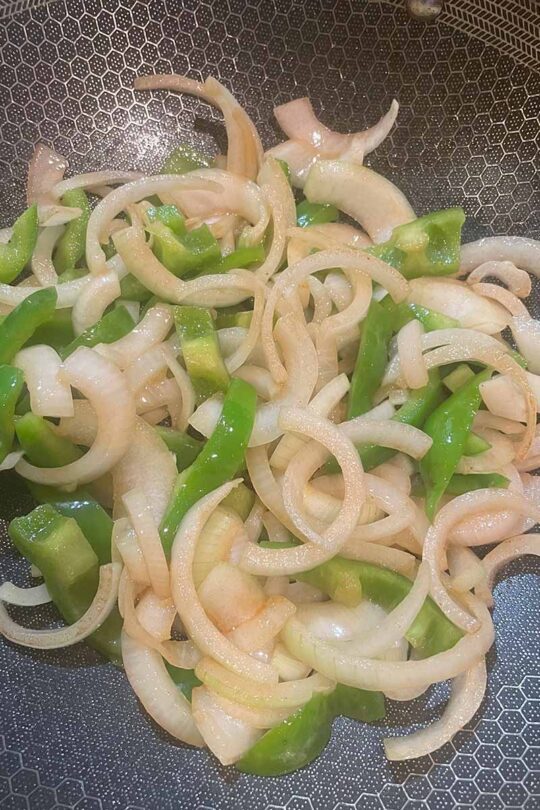 Sliced bell peppers and onions, being stir fried in wok.