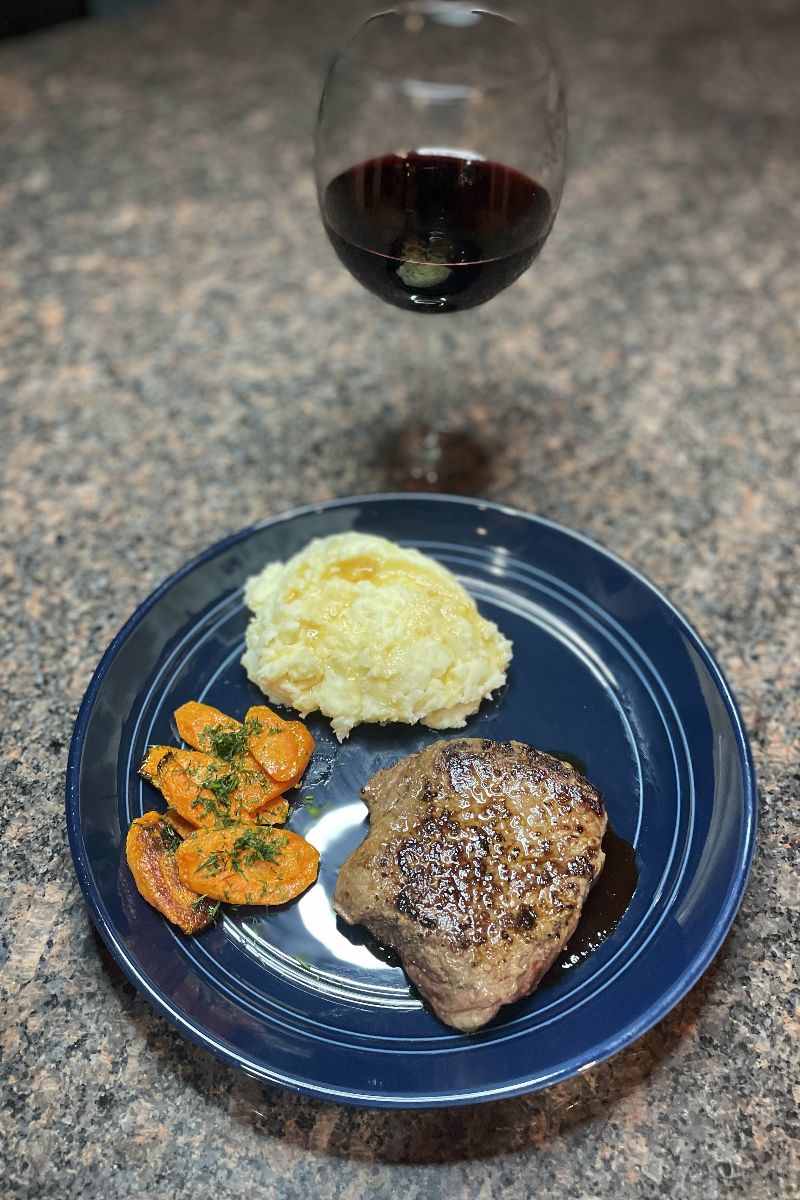 Home Chef meal of steak, mashed potatoes, and carrots on a plate next to a glass of wine.