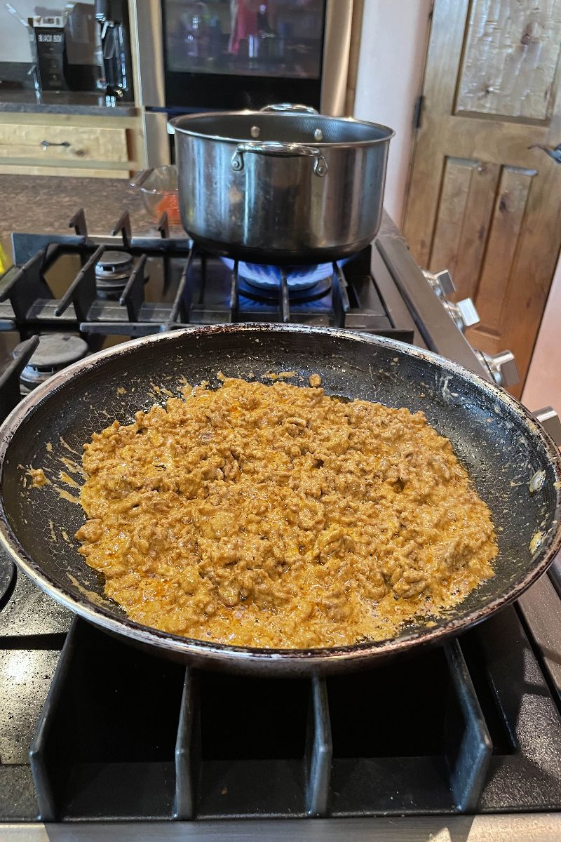 Ground beef mixed with cream cheese in a skillet.