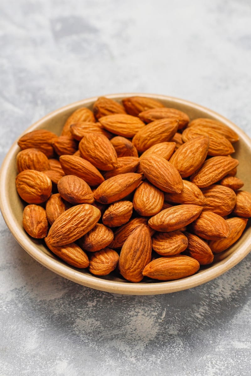 Bowl of roasted almonds on gray surface. 