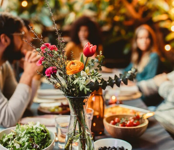 Friends eating dinner at table with flowers and food.