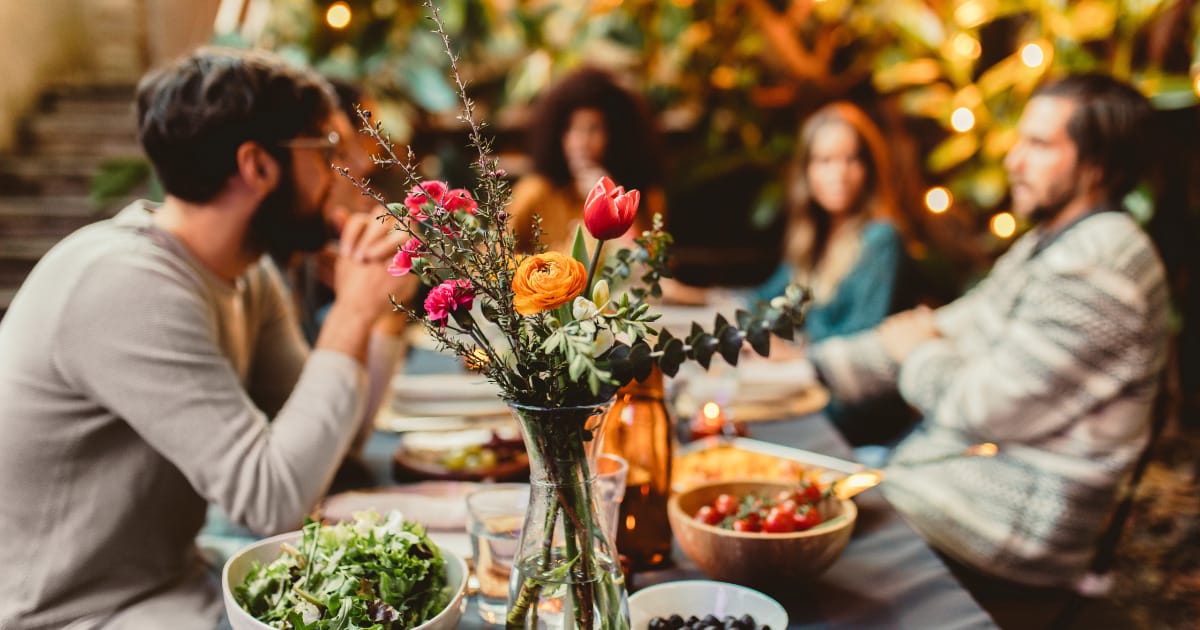 Friends eating dinner at table with flowers and food.