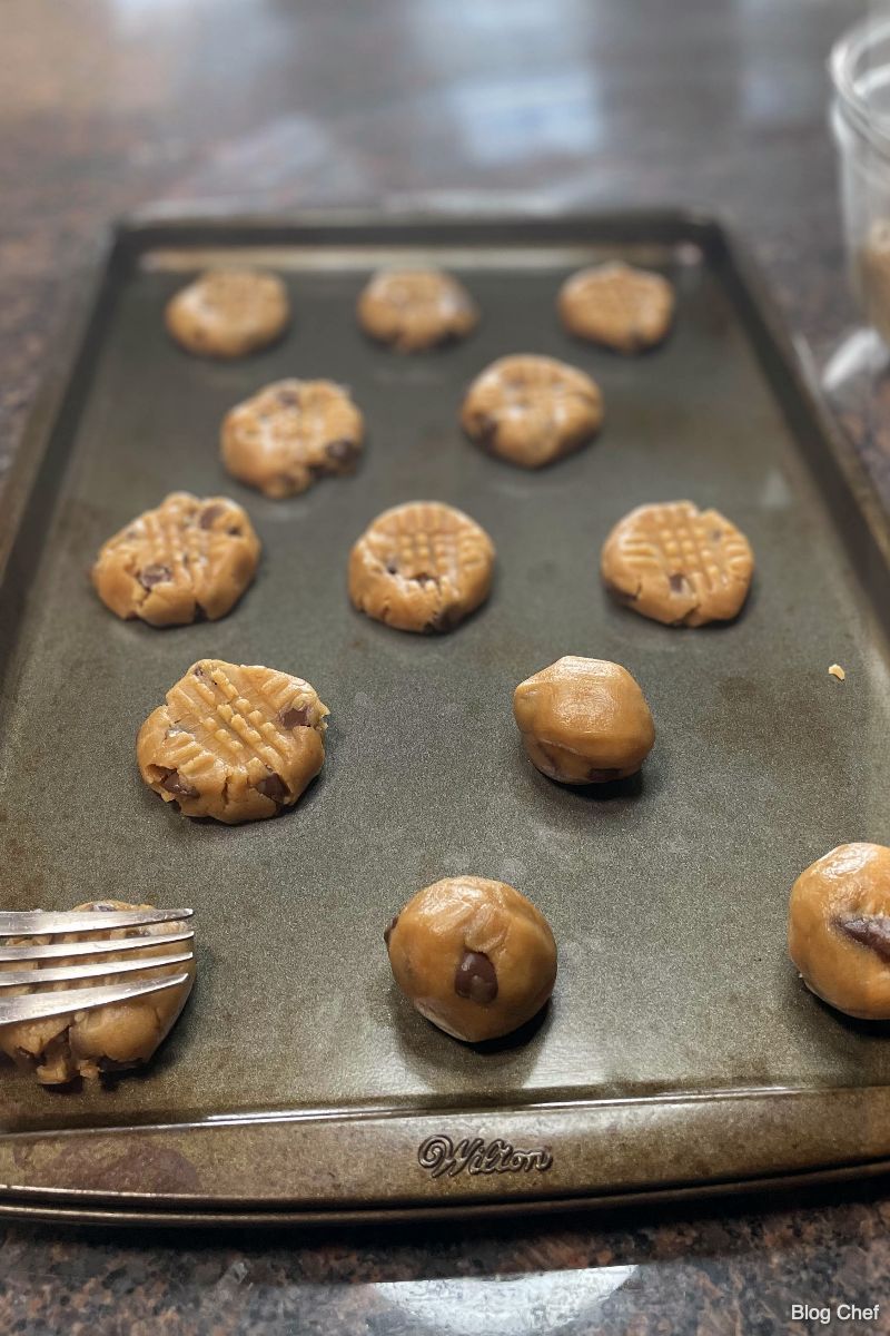 Flattening cookie dough with fork on baking sheet.