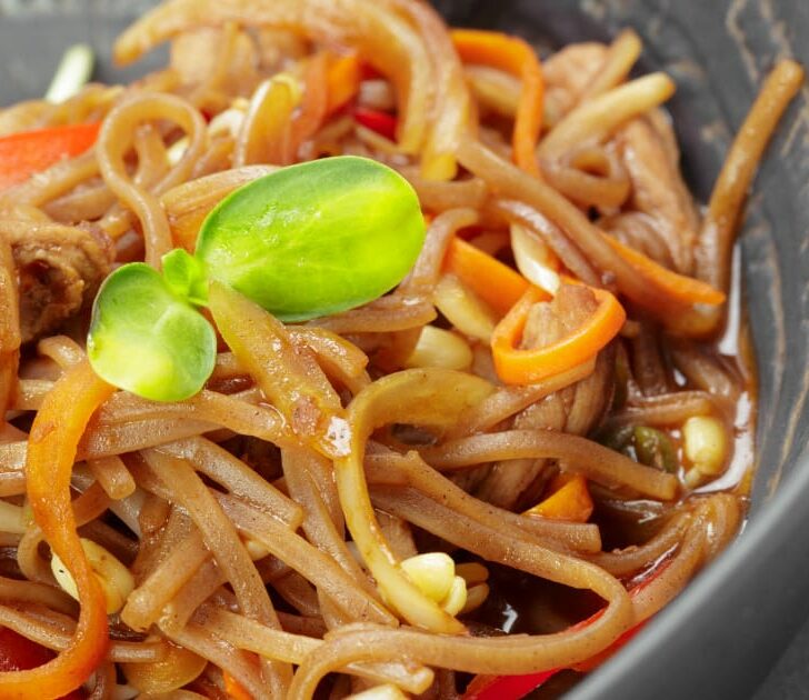 Close-up view of Asian noodles with shredded carrots and meat.