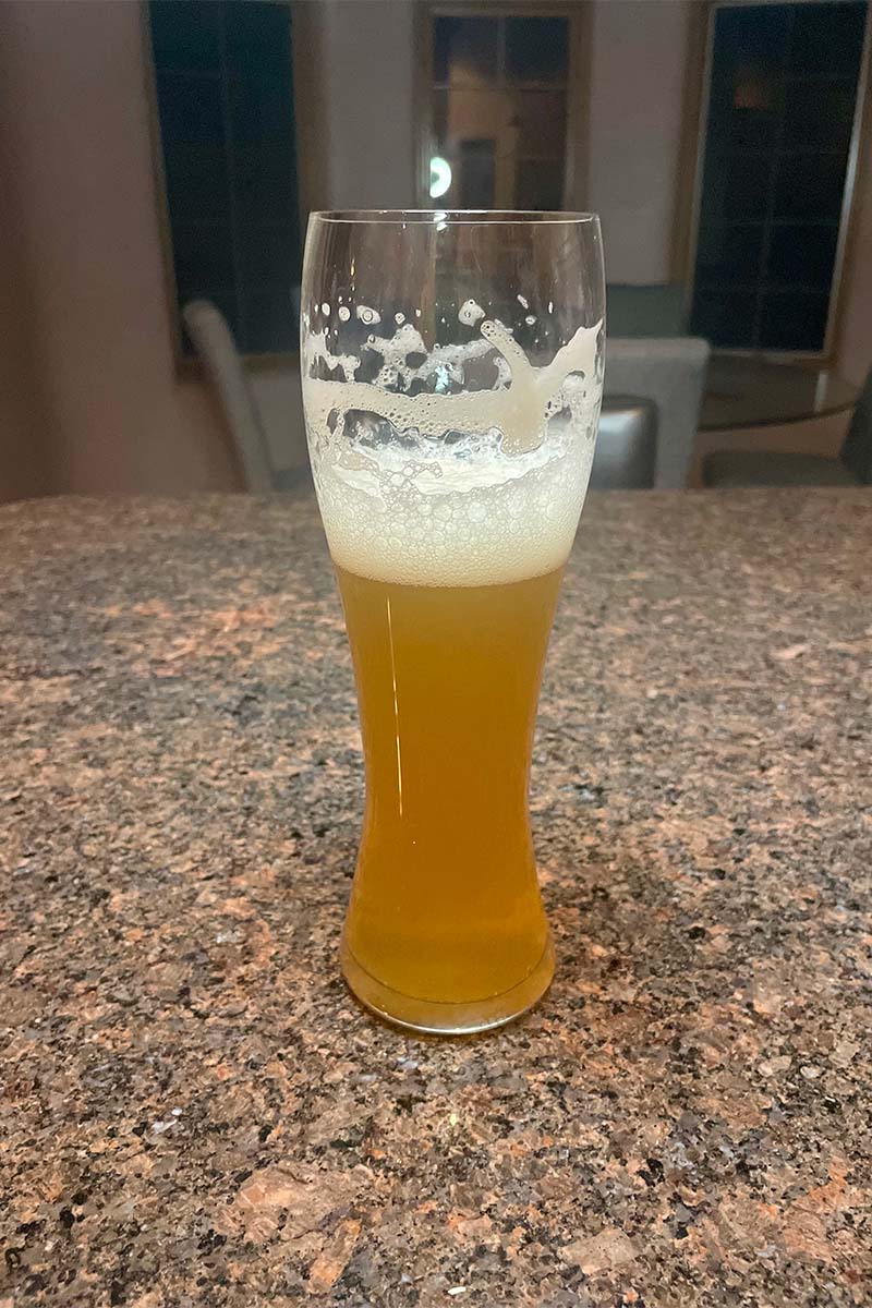 Glass of beer with foamy head on countertop.