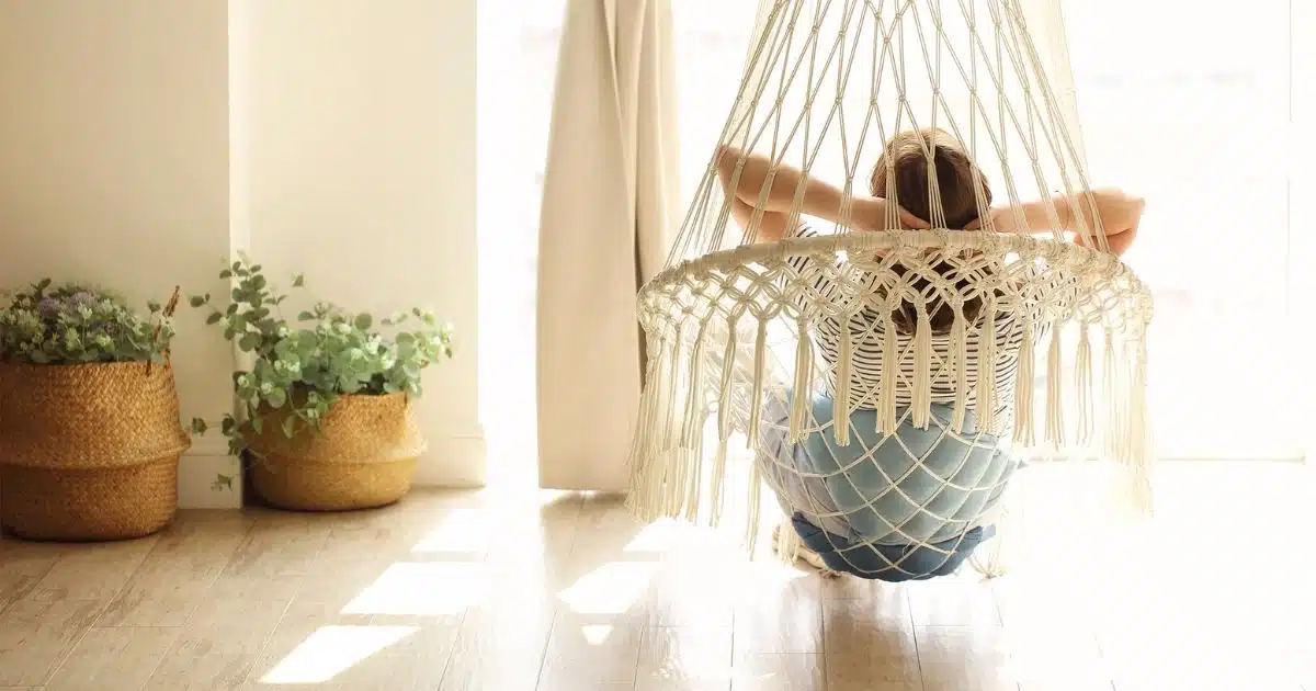 Woman sitting inside neutral-toned room in a hammock.