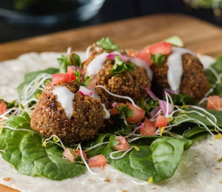 Falafel on tortilla with lettuce, tomatoes and sauce.