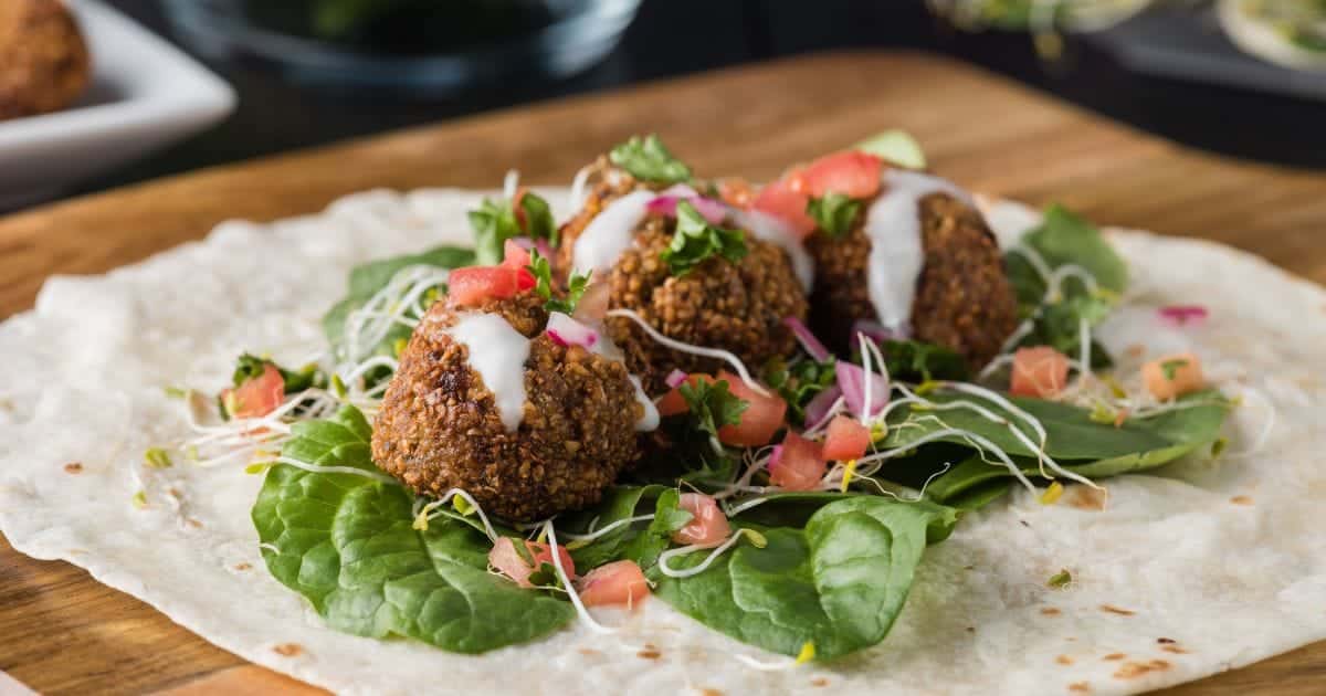 Falafel on tortilla with lettuce, tomatoes and sauce.