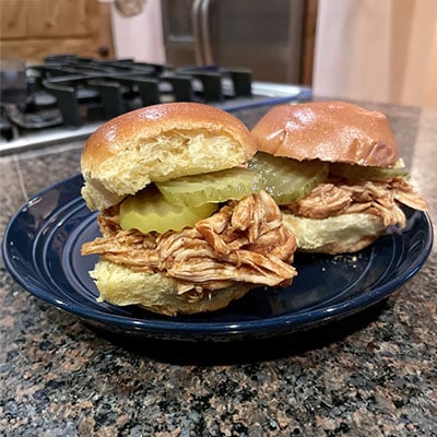 Slow cooker pulled chicken prepared in slider buns with pickles.