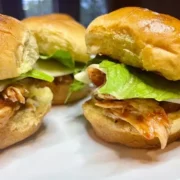 Prepared BBQ chicken sliders on white plate.