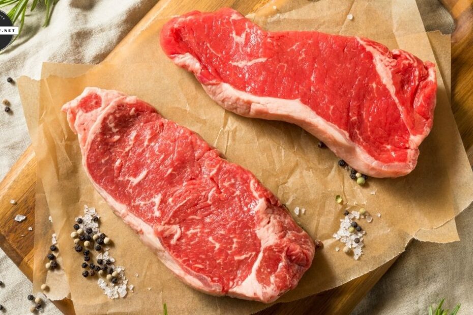 Raw grass fed beef steaks on parchment with rosemary and peppercorns