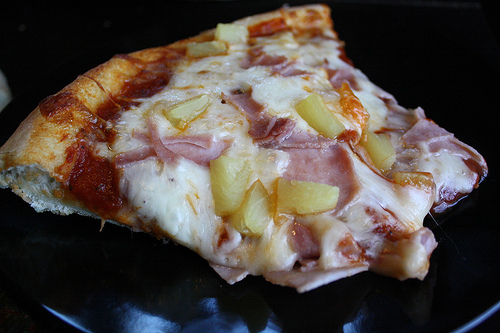 Slice of Hawaiian pizza on black plate