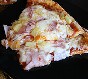 Slice of Hawaiian pizza on black plate