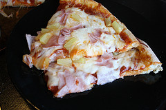 Slice of Hawaiian pizza on black plate