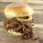 BBQ pulled beef sandwich with crispy onions on a wooden board